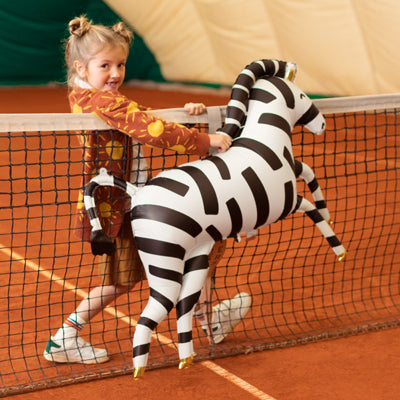Kind mit XXL Zebra-Folienballon von PartyDeco auf einem Tennisplatz
