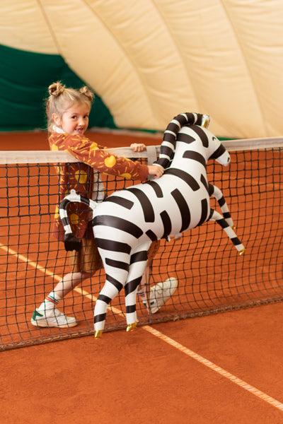 Kind mit XXL Zebra-Folienballon von PartyDeco auf einem Tennisplatz